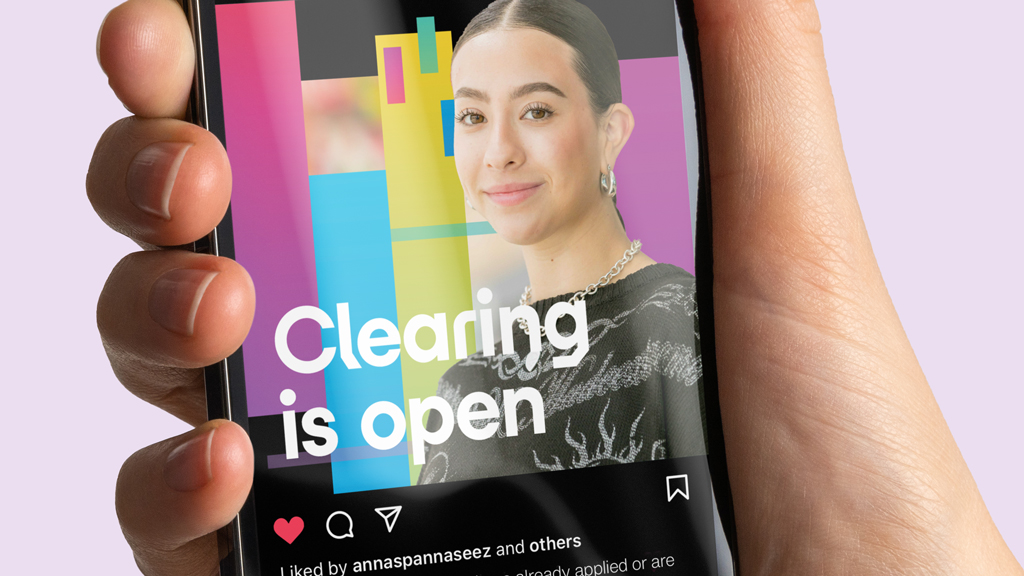 A hand holding an iPhone displaying an Instagram post from the University of Hertfordshire